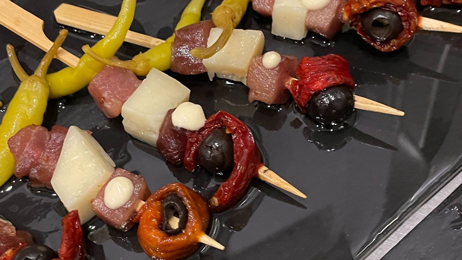 Brochetas con dados de atún curado, queso semicurado, piparras, aceitunas negras y tomates secos.