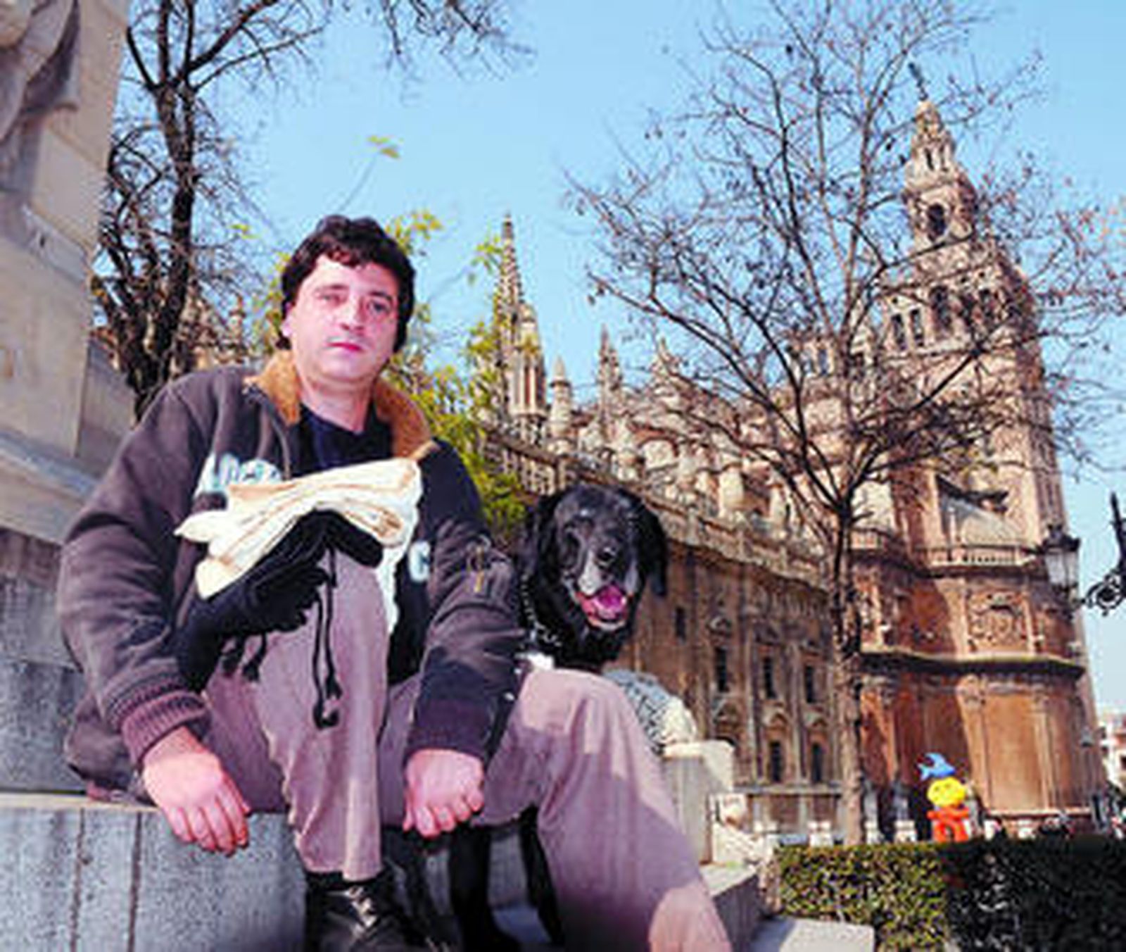 Antonio Manuel Ares, con la ropa de costalero y su perra guía en la Plaza del Triunfo.