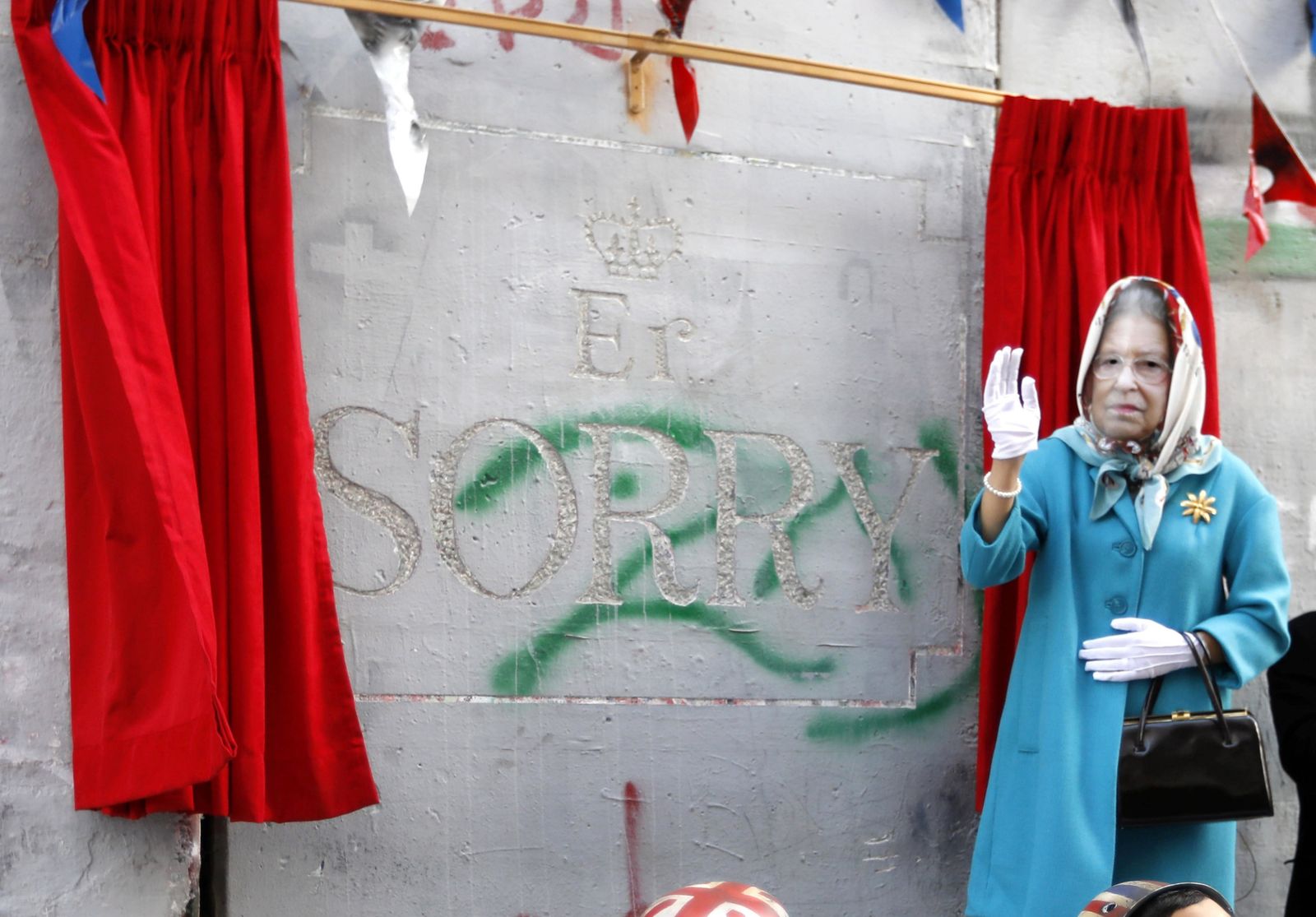 Una mujer con una careta de Isabel II tras descubrir el trozo de muro tallado para la ocasión.
