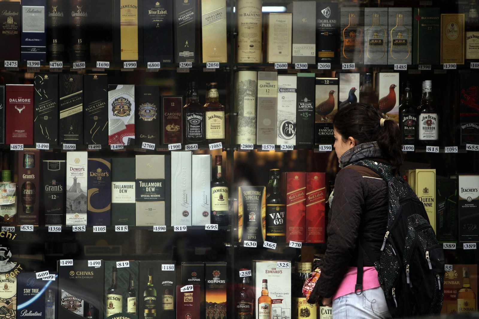 Una mujer pasa por delante de una vitrina de una tienda de licores.