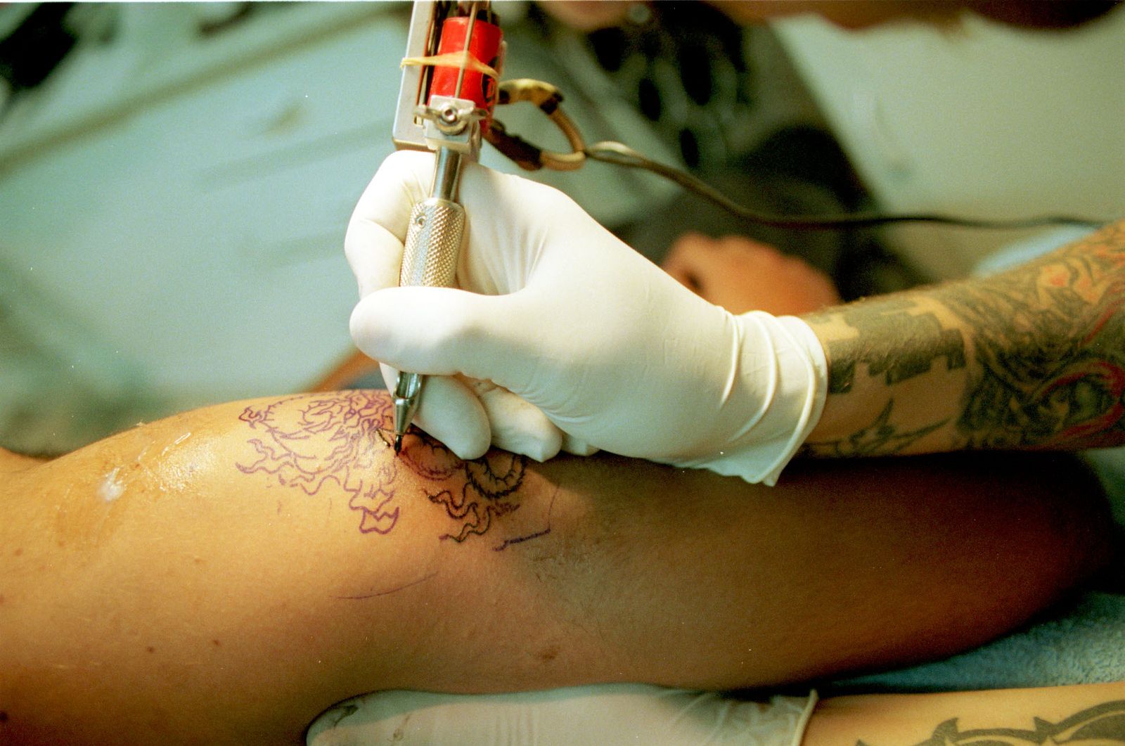 Un tatuador realiza un dibujo en el brazo de un joven.