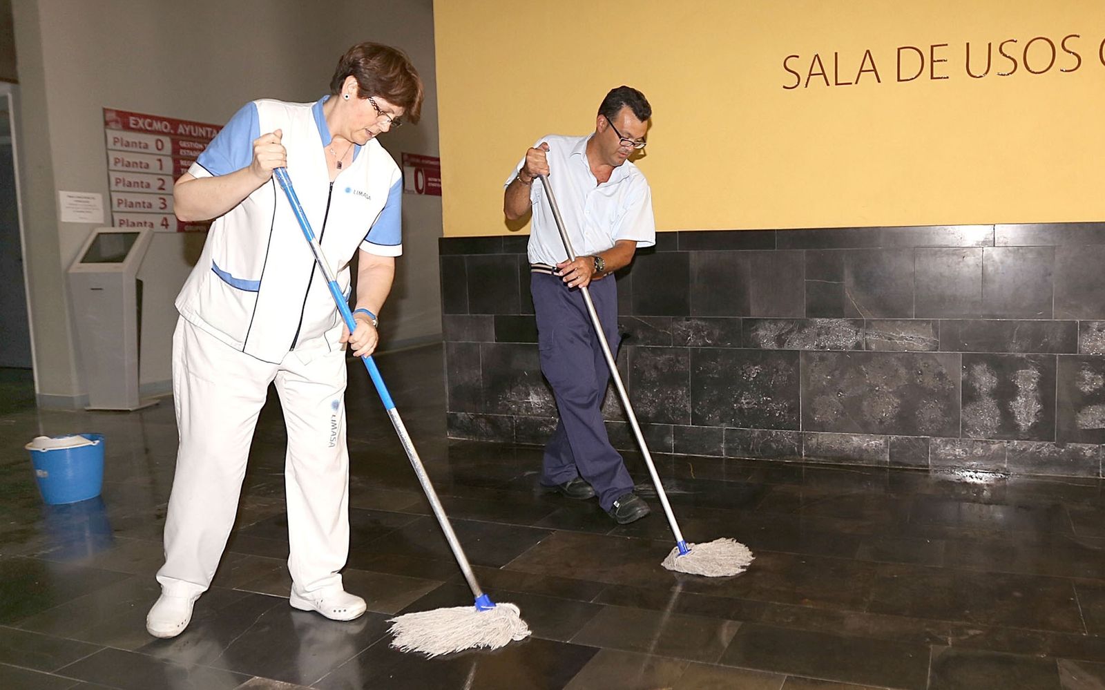 Una mujer y un hombre realizan labores de limpieza en un edificio.