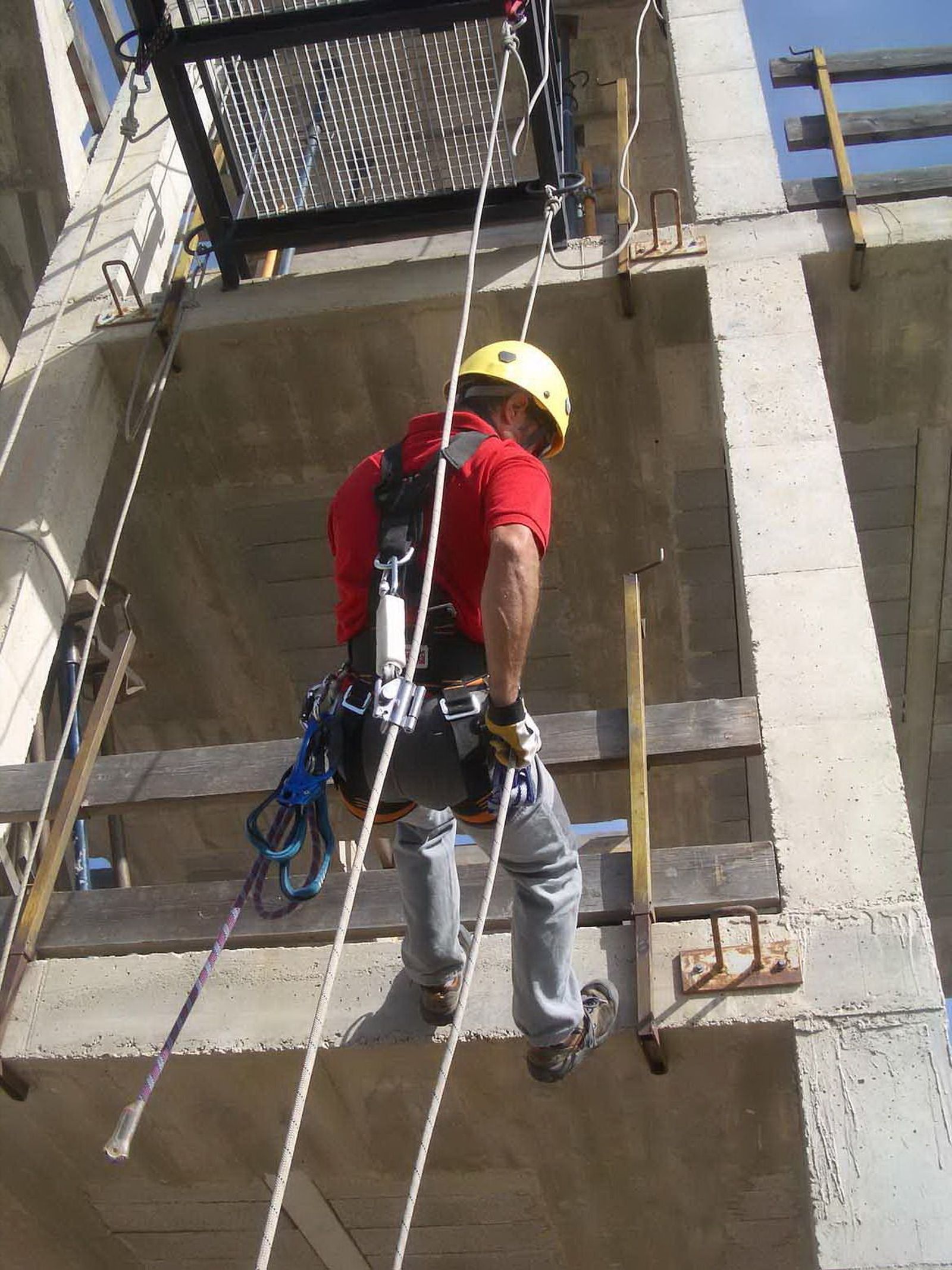 Un trabajador de una obra usando el arnés y sujeciones para prevenir riesgo de caídas.