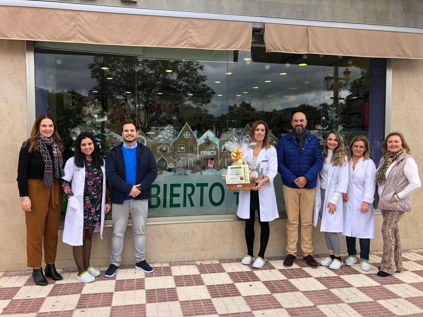 Las autoridades municipales y el personal de la Farmacia Peña Marín junto al escaparate.