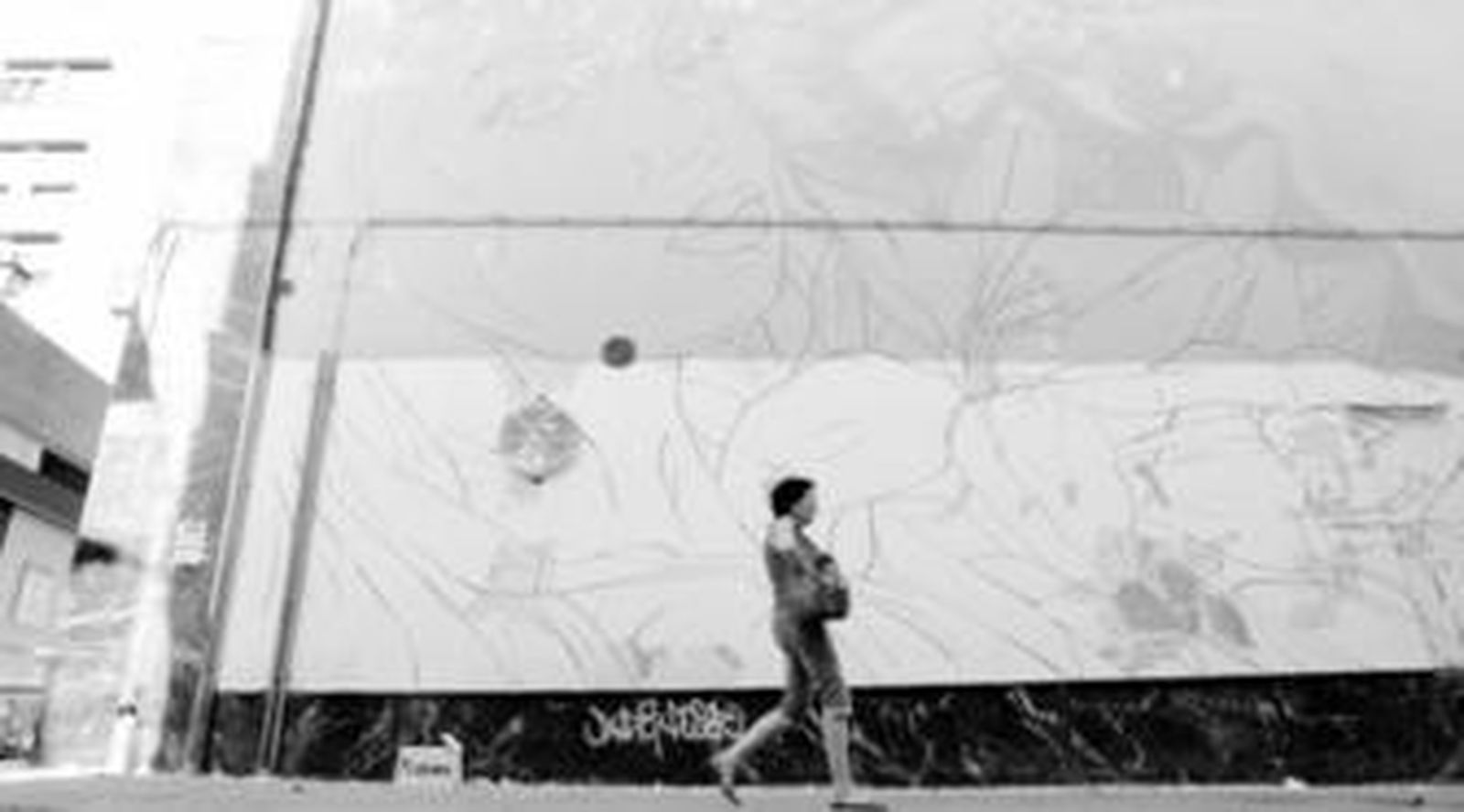 Una mujer cruza por delante del mural sobre el que Daniel Fernández trabaja a contrarreloj para tenerlo concluido antes de Feria.