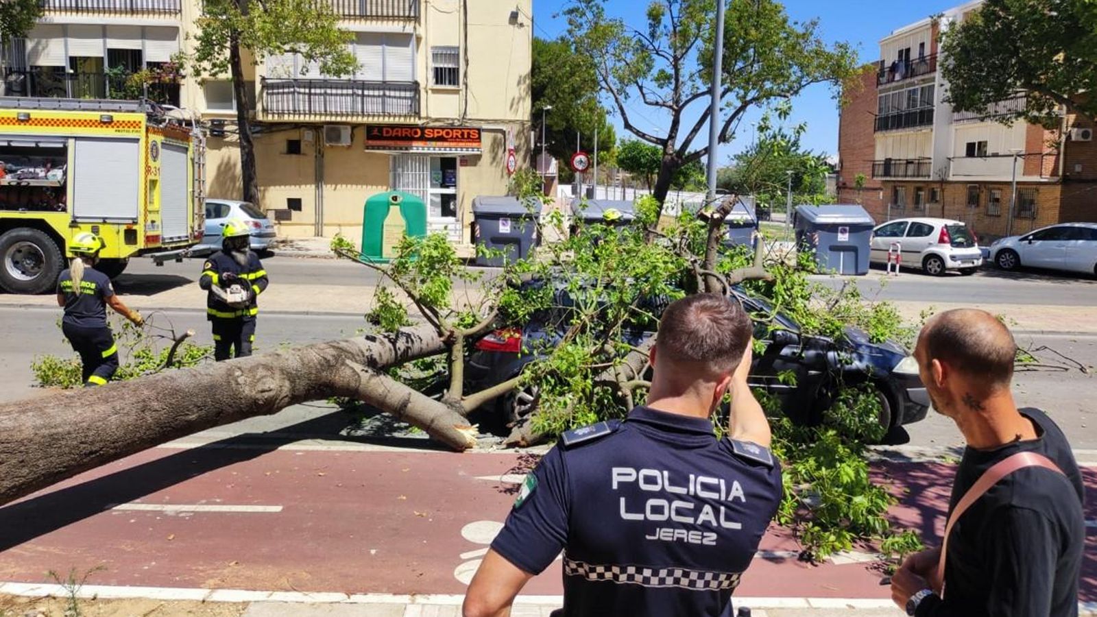 Un agente de la Policía Local conversa con un vecino mientras los bomberos despejan la zona.