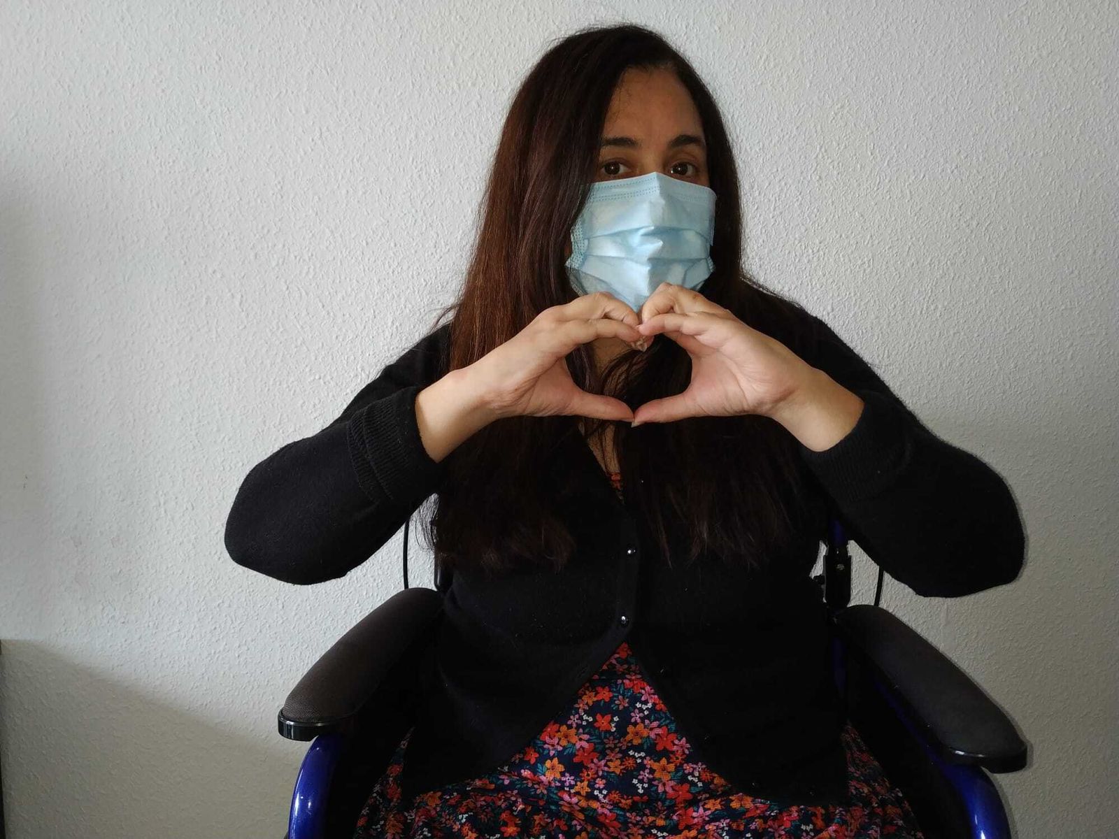 Gema, sevillana que padece una enfermedad neuromuscular, hace el gesto del corazón en el Día Mundial dedicado a estas patologías raras.