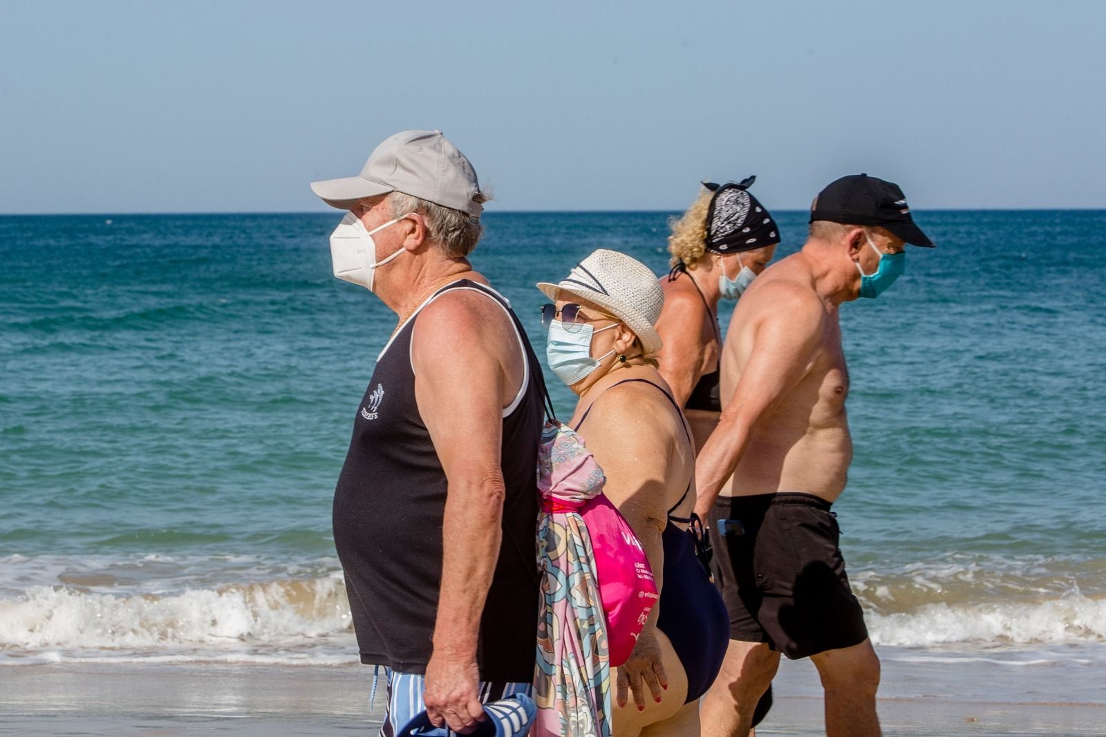 Personas mayores paseando por la playa con sus mascarillas.