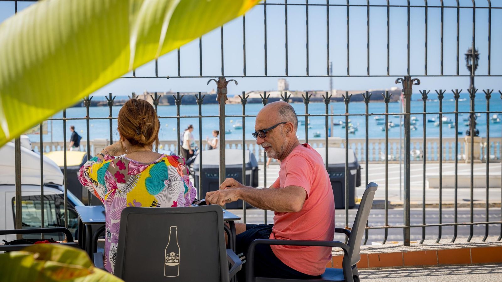 Una pareja desayuna con el castillo de San Sebastián al fondo.