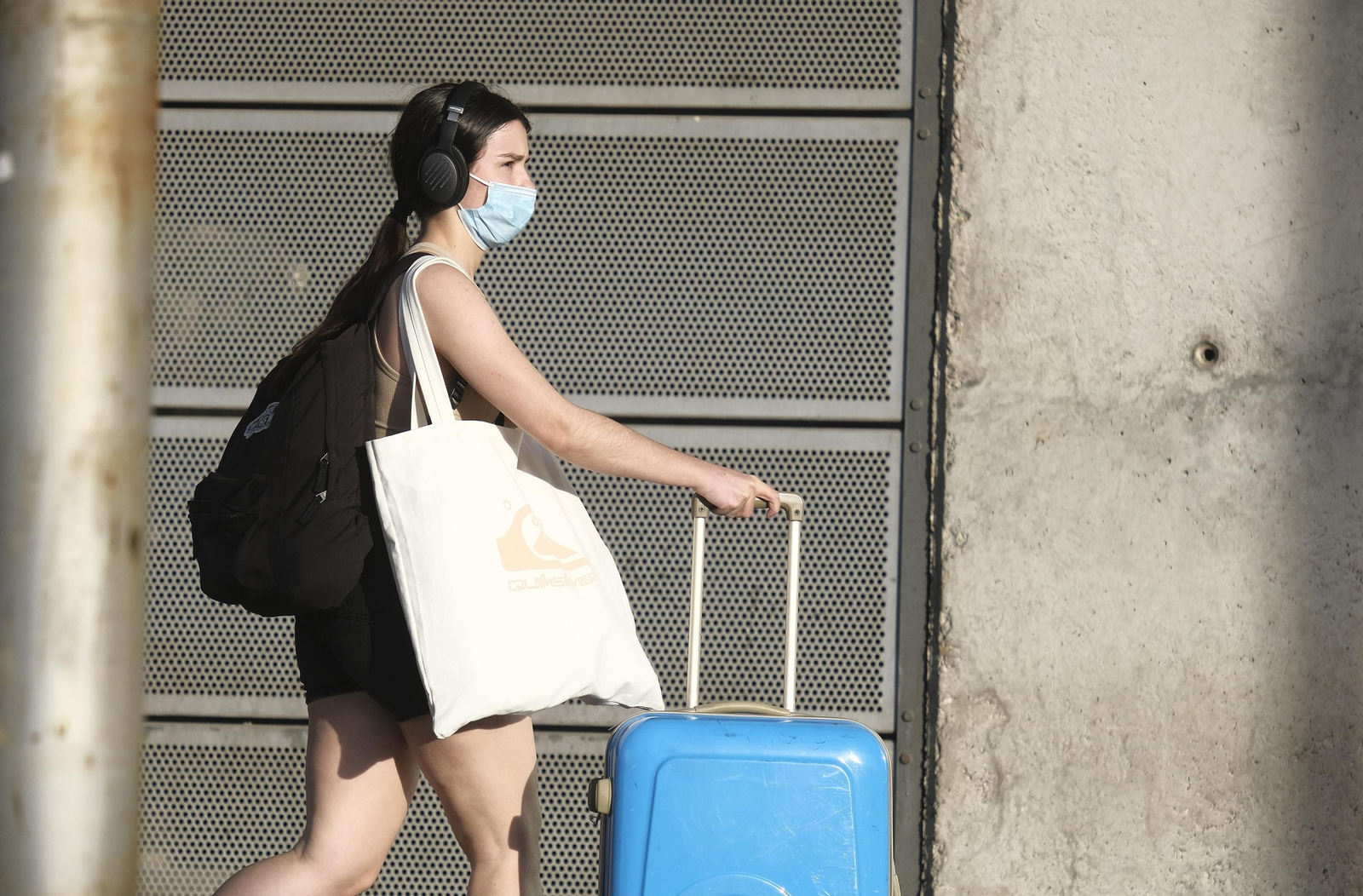 Una joven, protegida por su mascarilla, camina con su maleta por el entorno de la estación.