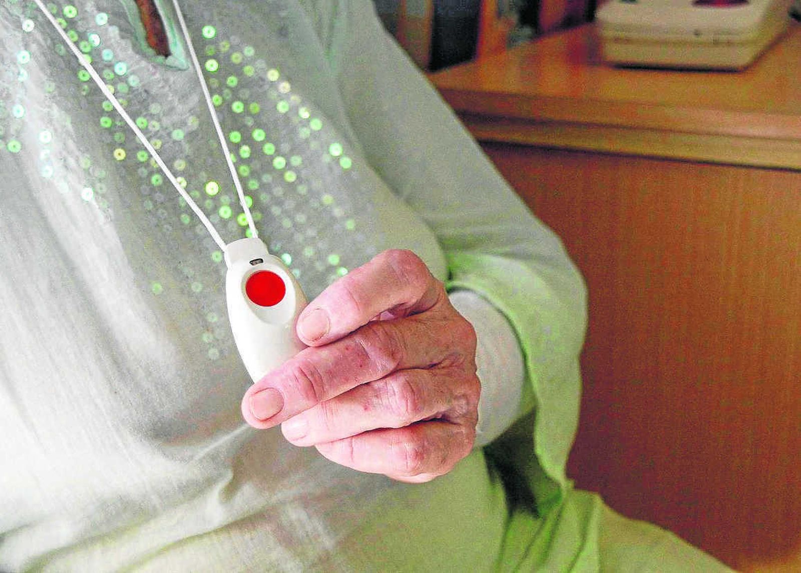 Una anciana muestra el dispositivo para pedir ayuda desde casa.