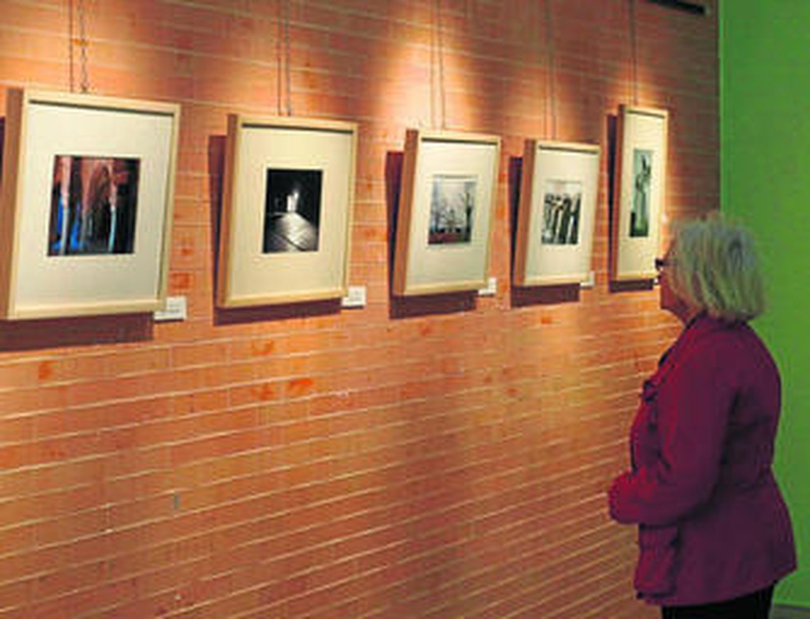 Una mujer mira algunas de las fotografías de la exposición. Abajo, el alcalde de Aljaraque, David Toscano.