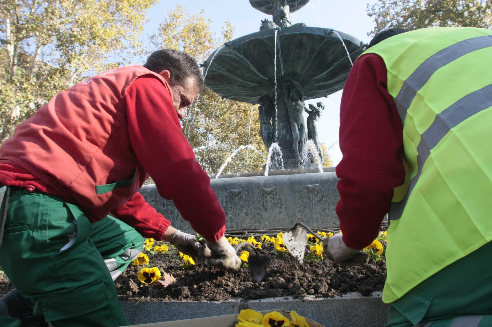 Dos operarios cambian las flores de la Fuente de las Batallas.