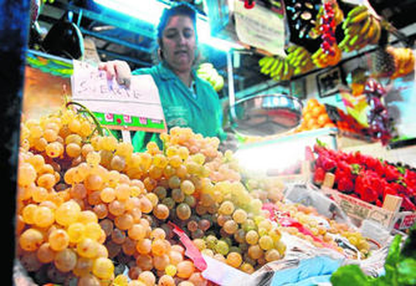 Una tendera coloca un cartel entre los racimos de uva, ayer en la plaza de abastos.