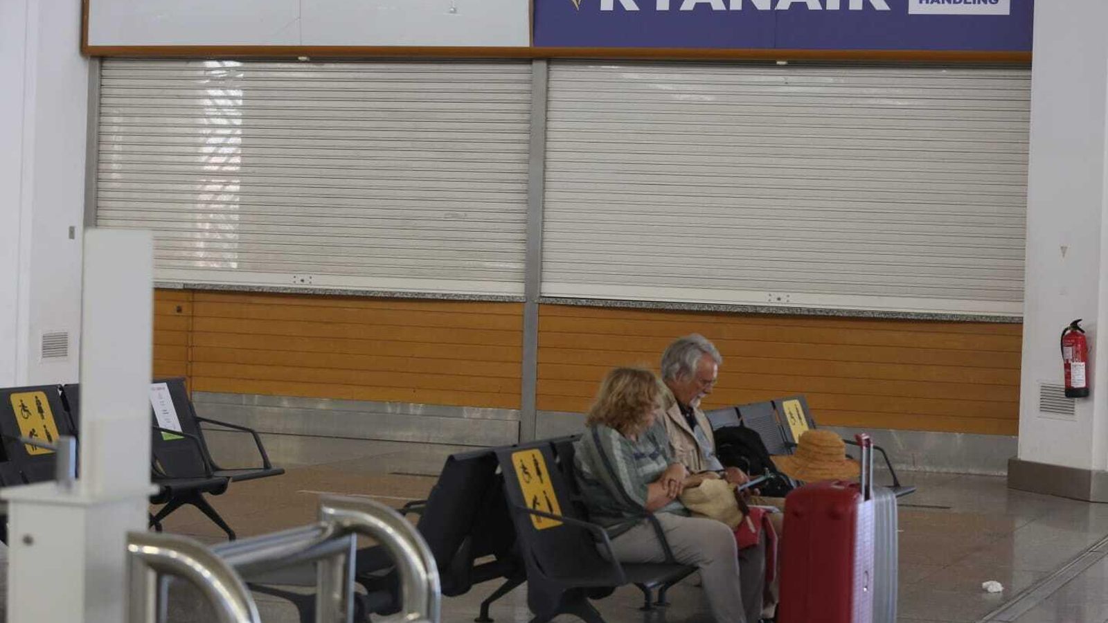 Una pareja sentada, junto a su equipaje, a las puertas de una oficina de Ryanair.