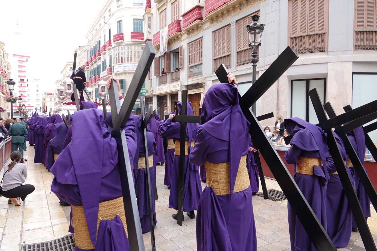 Nazarenos cargados con cruces siguen a Nuestro Padre Jesús de la Pasión en la calle Larios.