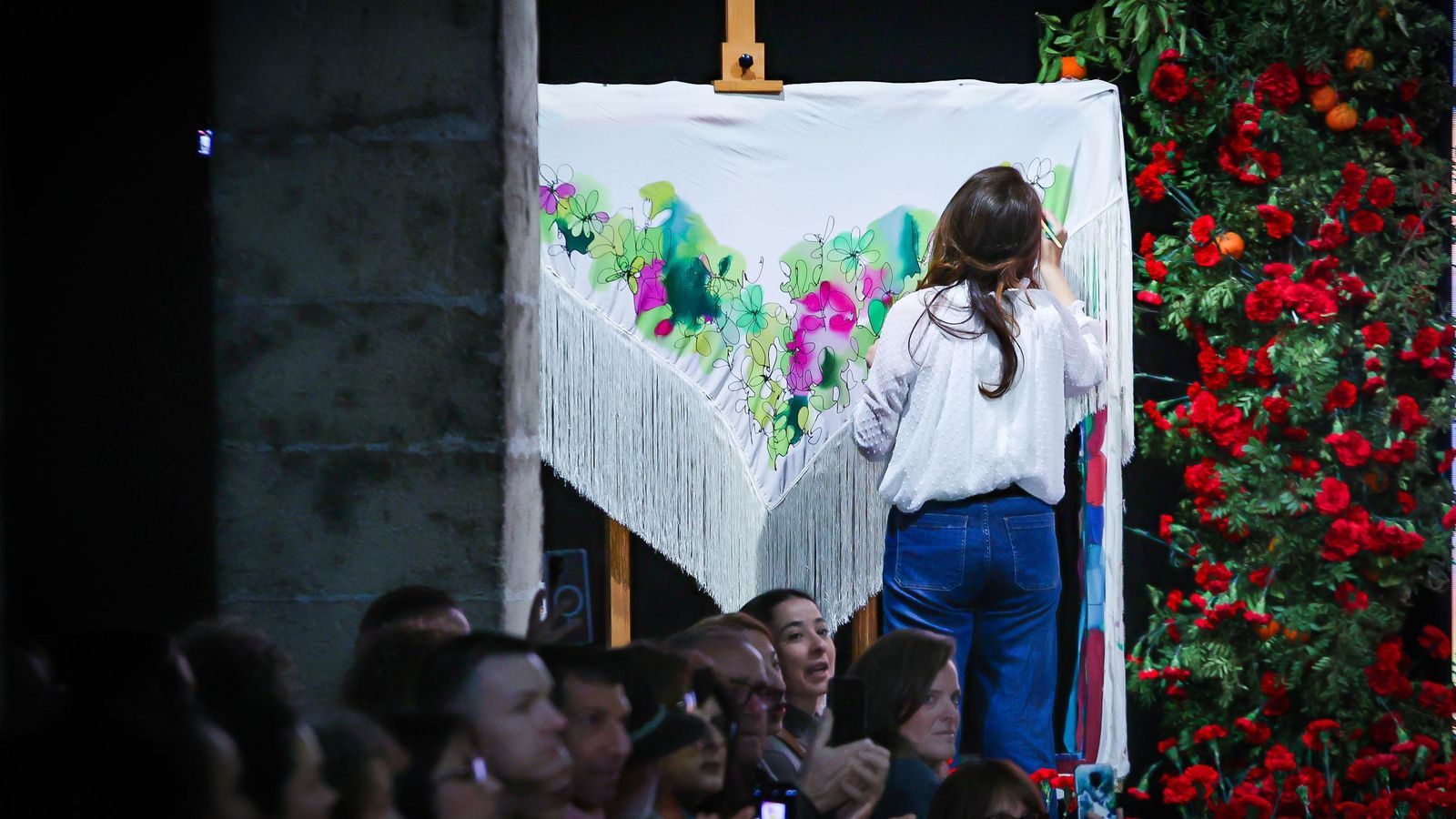 Belén González García-Negrotto, hija del artista Luis Gonzalo, pintando un mantón de seda sobre el escenario durante el desfile.