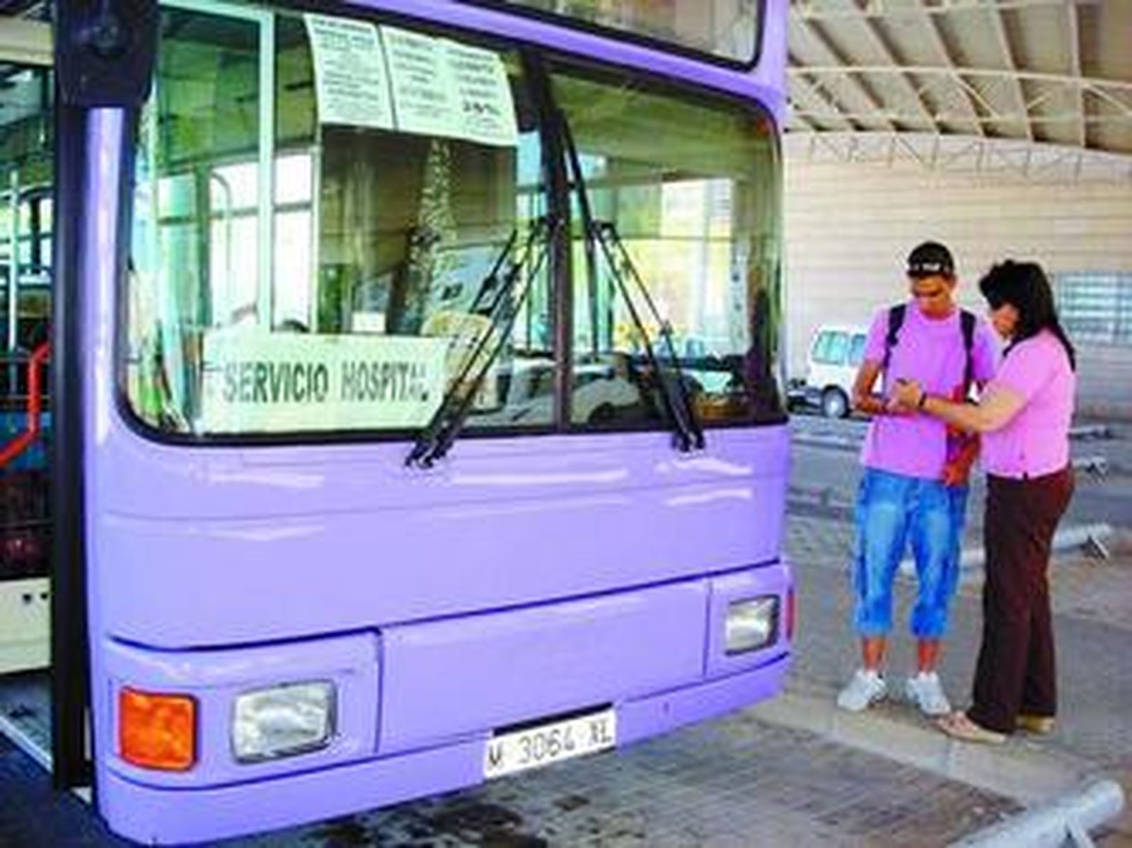 Dos viajeros esperan para montar en un autobús urbano que se encuentra estacionado en la estación.