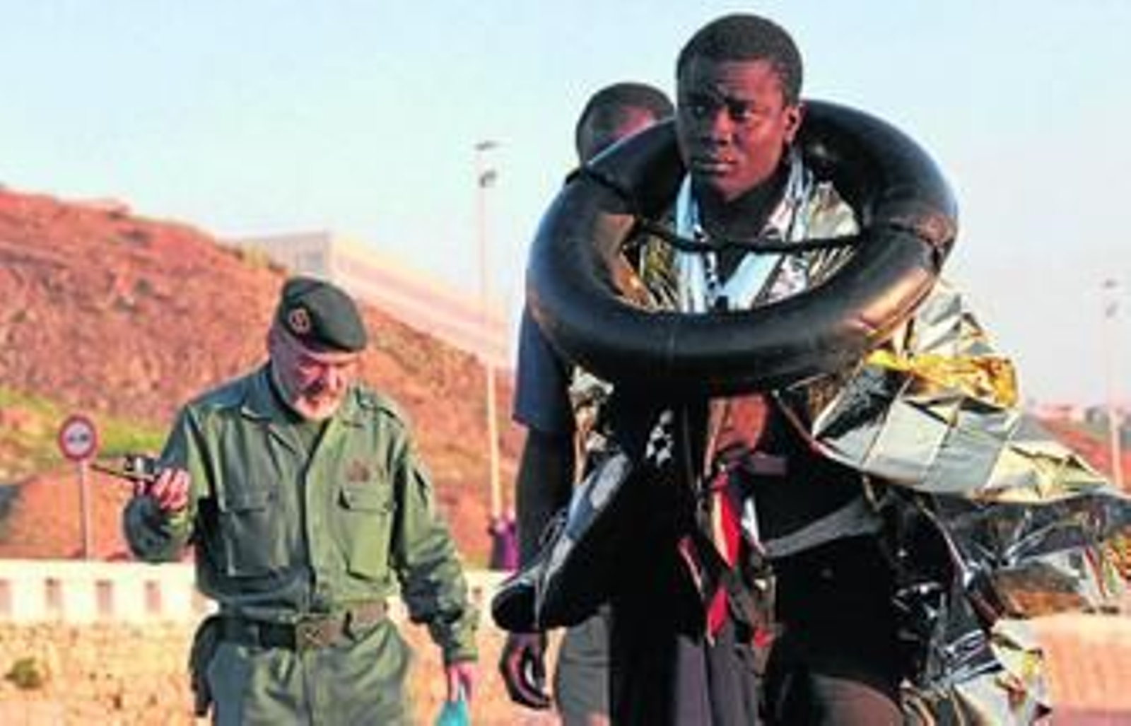 Un guardia civil acompaña a dos inmigrantes subsaharianos en una playa de Ceuta próxima a la frontera con Marruecos, en una imagen de archivo.