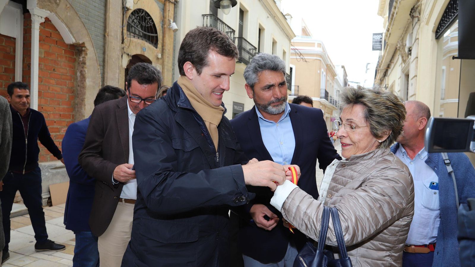Pablo Casado le pone una pulsera con los colores de España a una señora.