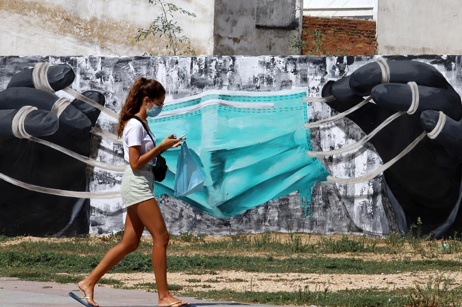 Una joven paseando por Huelva ante un muro en el que han dibujado una gran mascarilla.
