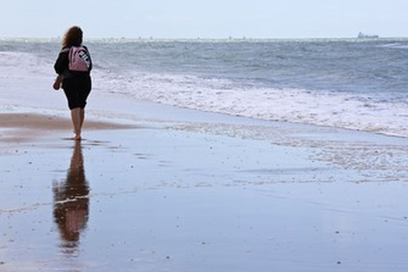 Una chica pasea por la orilla de la playa.