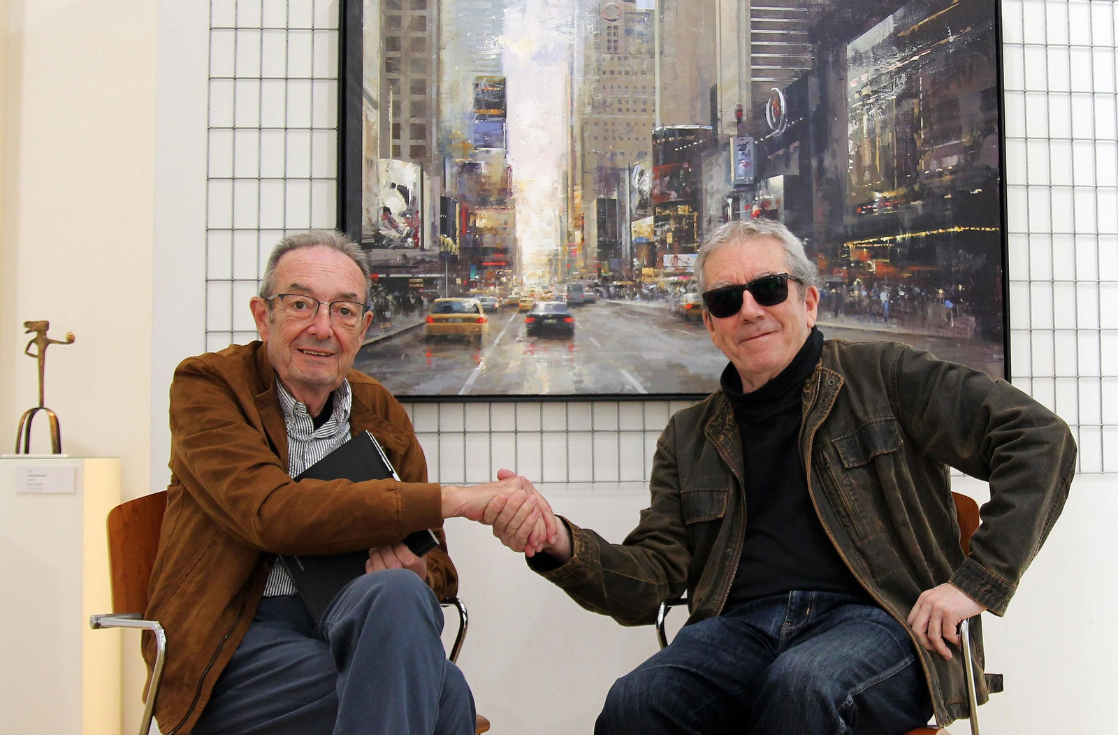 Rafael Benot y Ricardo Galán Urréjola posan en la Galería Benot, ante una de las grandes urbes del pintor