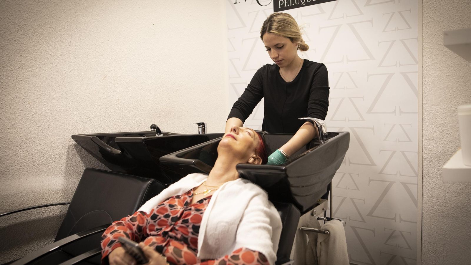 Una empleada de una peluquería lava el pelo a una clienta, ambas sin mascarilla