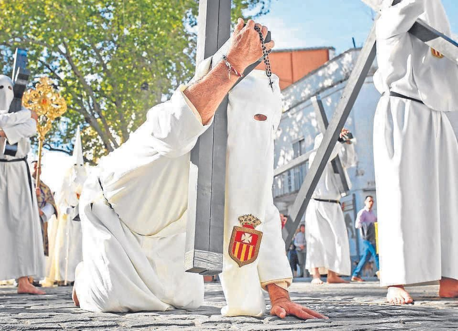 Un nazareno de la Hermandad del Transporte, arrodillado con la cruz al hombro a su paso por el barrio de Santiago.