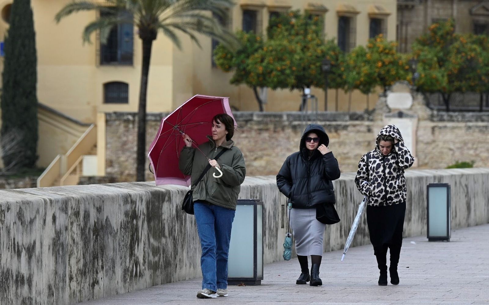 Unas mujeres se protegen de la lluvia y el viento en el Puente Romano.