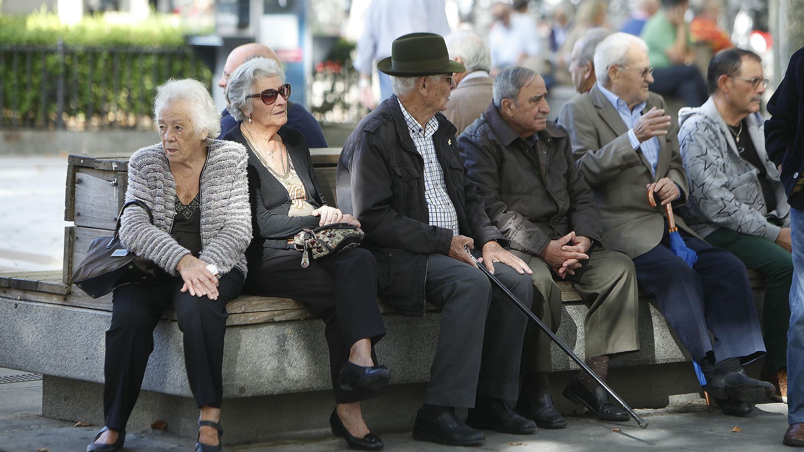 Varias personas mayores sentadas en un banco en la Plaza Nueva.