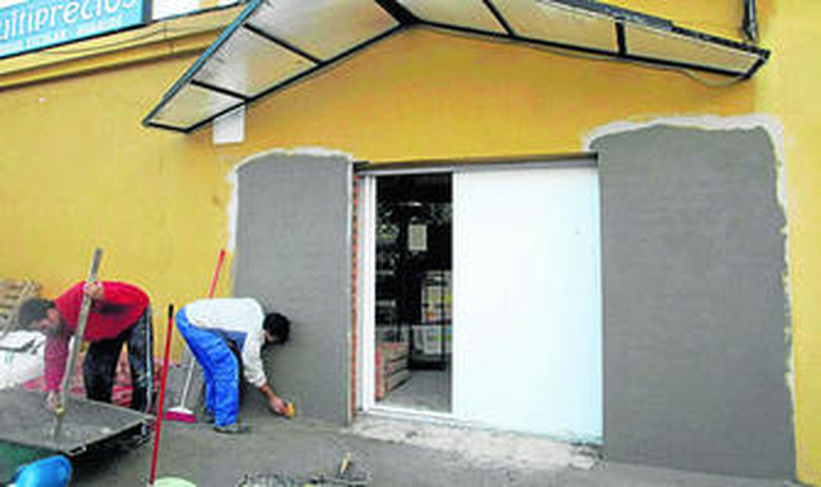 Unos trabajadores arreglan la entrada de la ferretería, ayer, tras los daños causados.