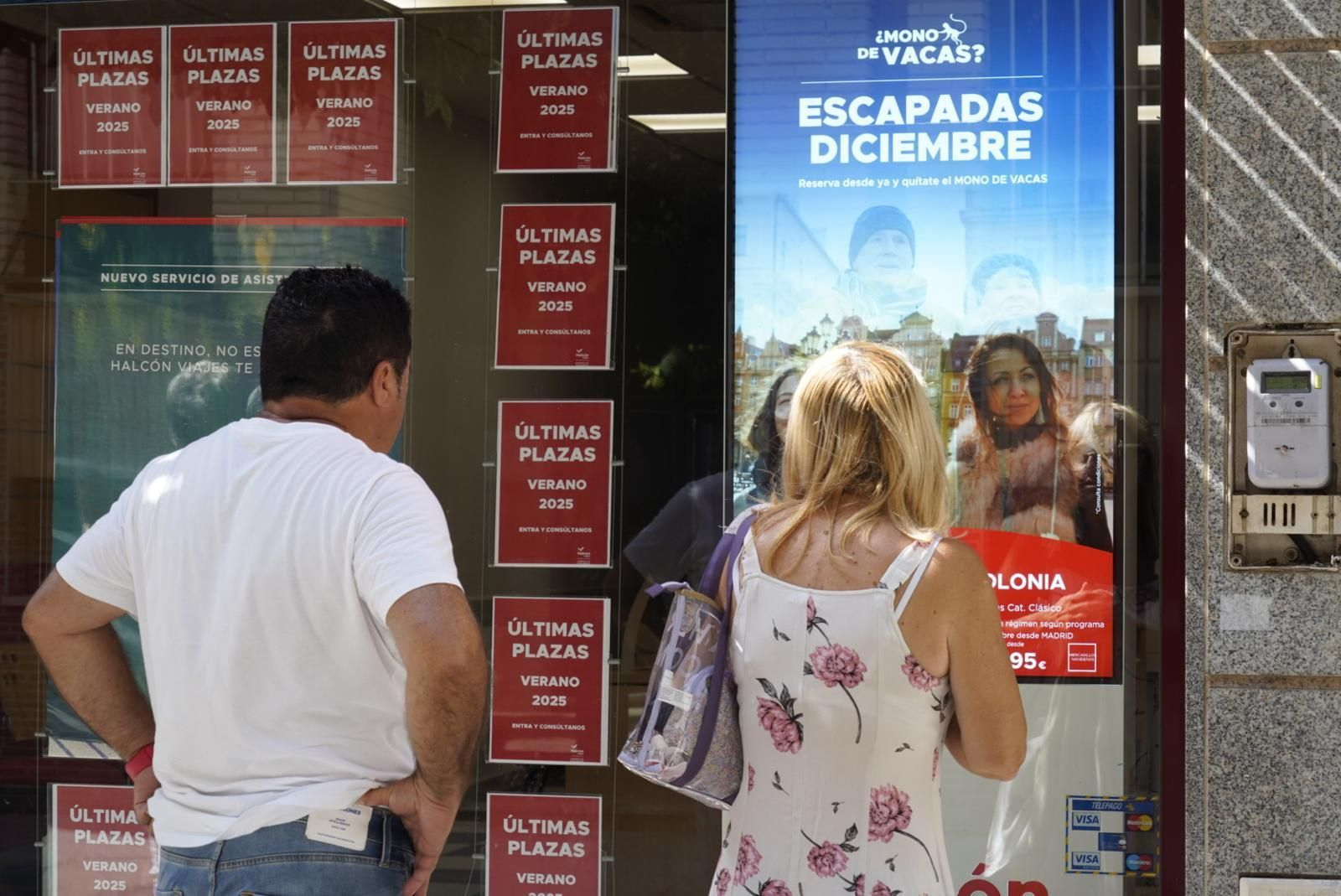Una pareja mira ofertas de viajes en el escaparate de una agencia.