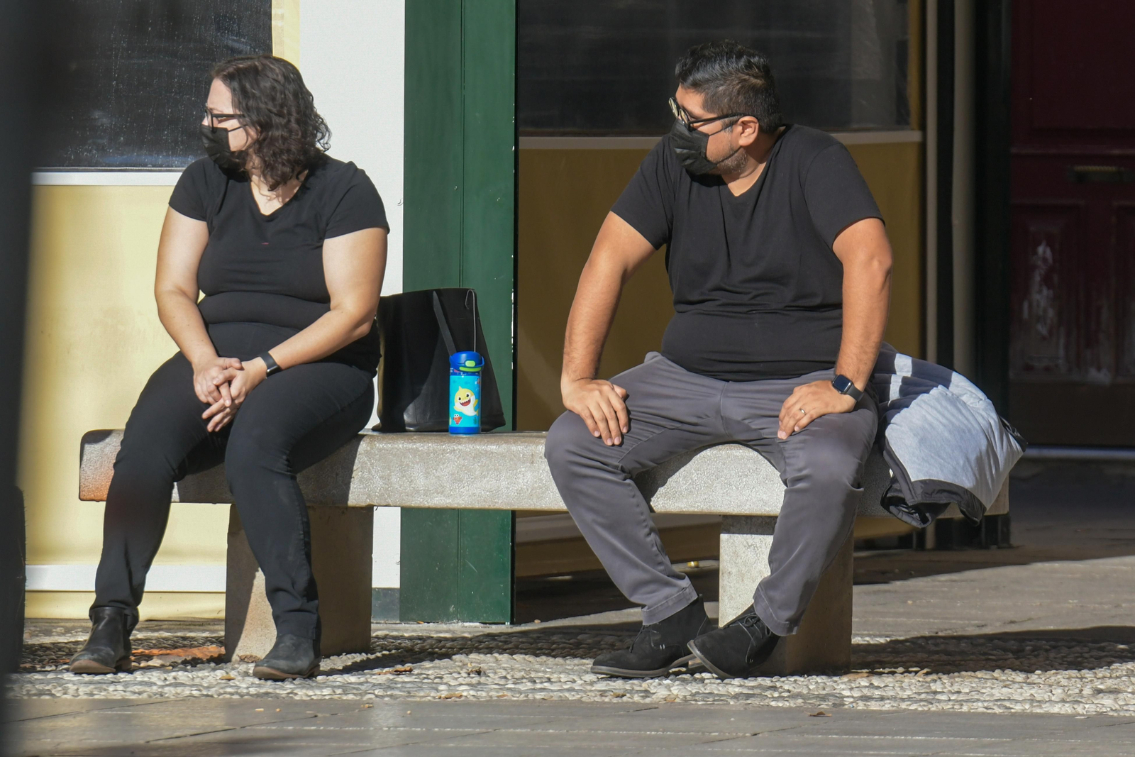 Dos personas, sentadas en un banco, con mascarillas.