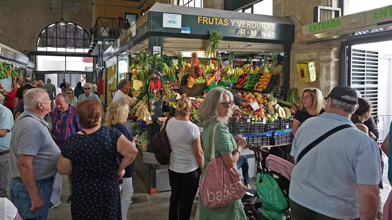 Consumidores junto a los puestos de frutas y verduras de un mercado de abastos.