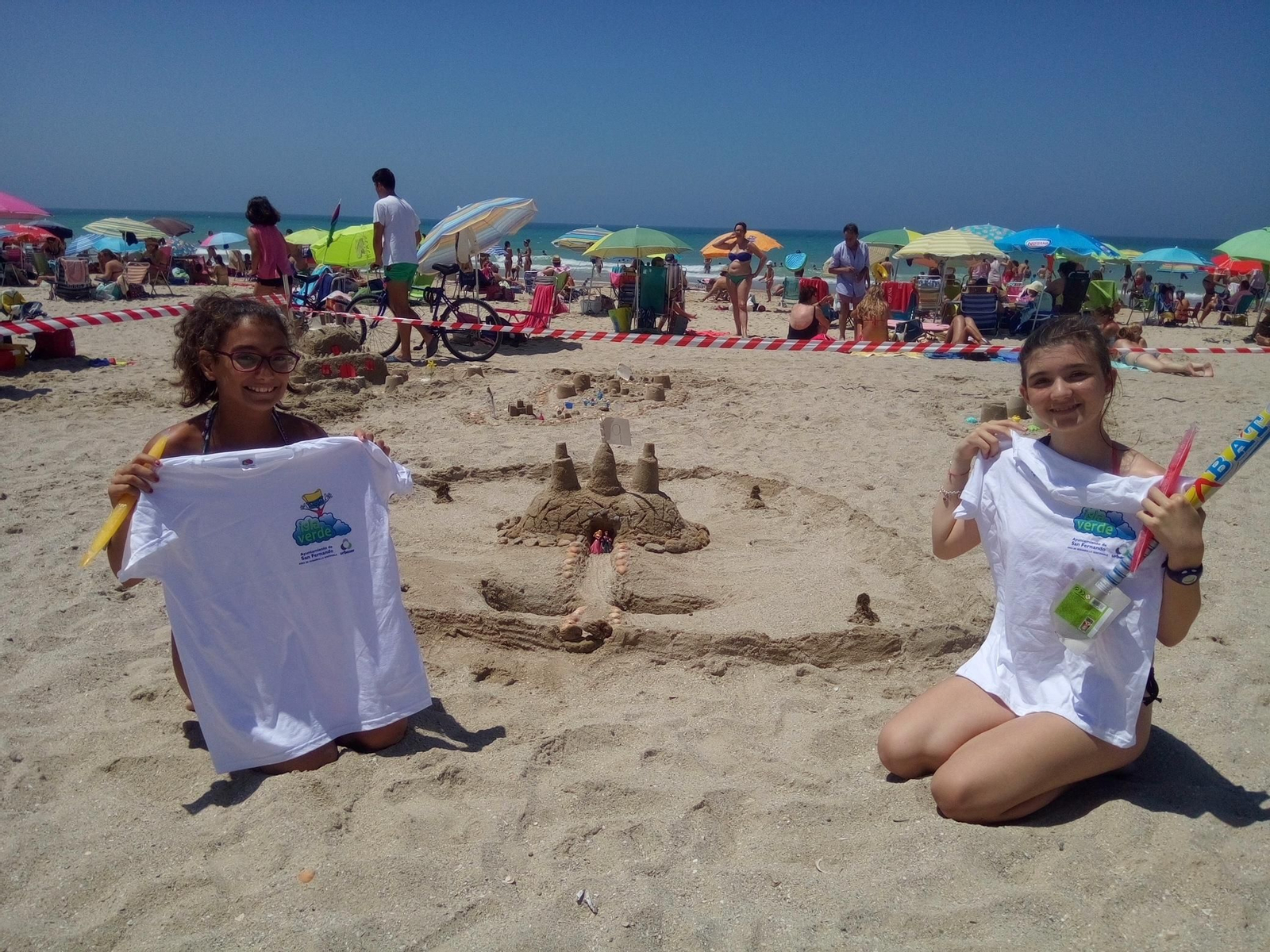 Dos chicas tras hacer un castillo en la arena con camisetas de Isla Verde.