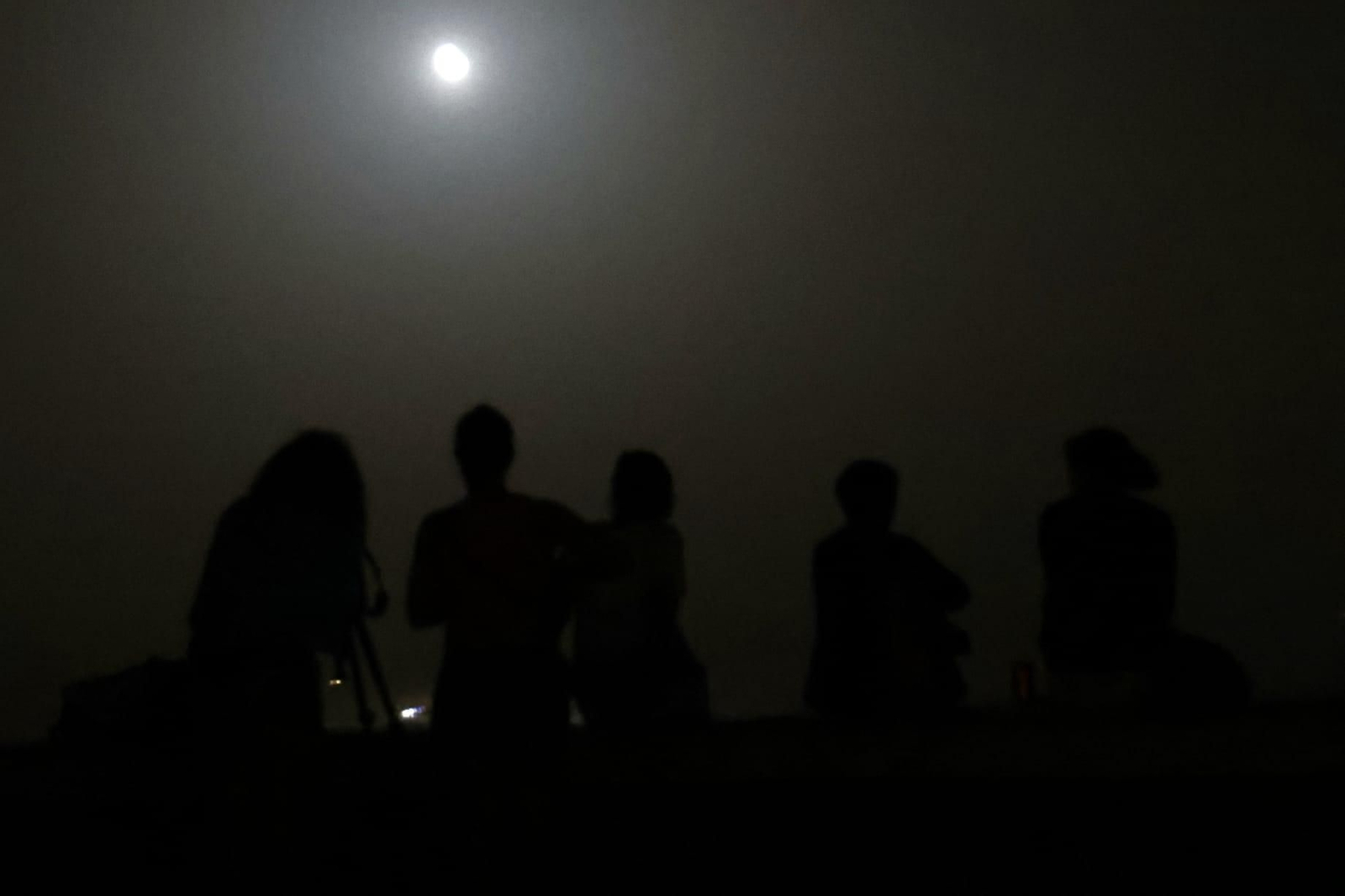 Varias personas contemplan la Luna desde Algeciras, este domingo.