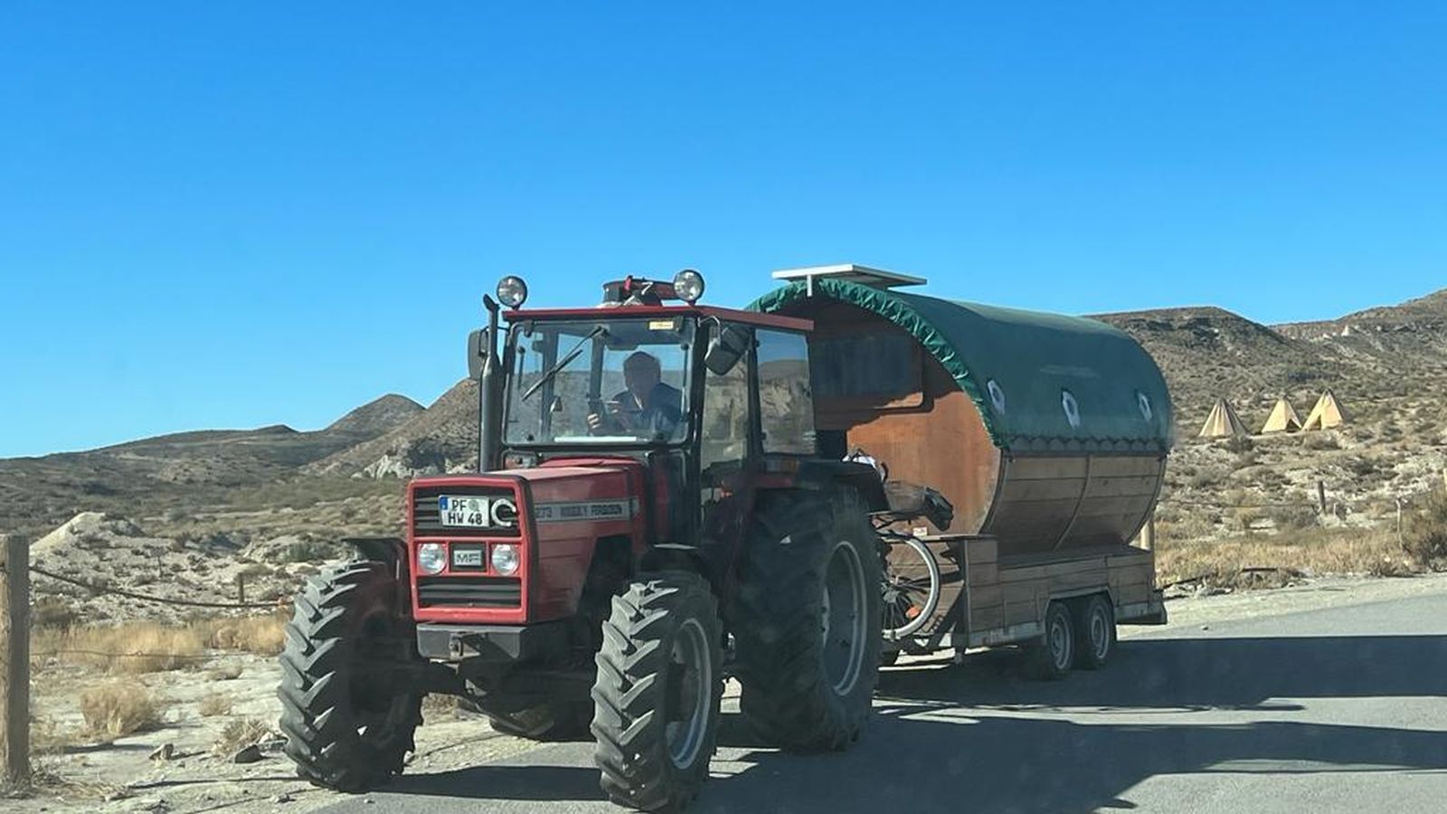 El tractor de Hubert tira de la caravana, una antigua sauna, con el poblado del oeste de Tabernas de fondo.