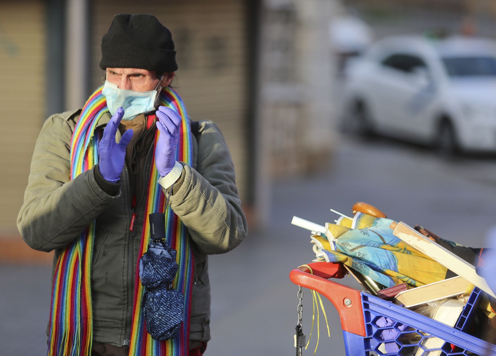 Un hombre que atesora objetos encontrados en un carrito de supermercado aplaude a los sanitarios en la calle.