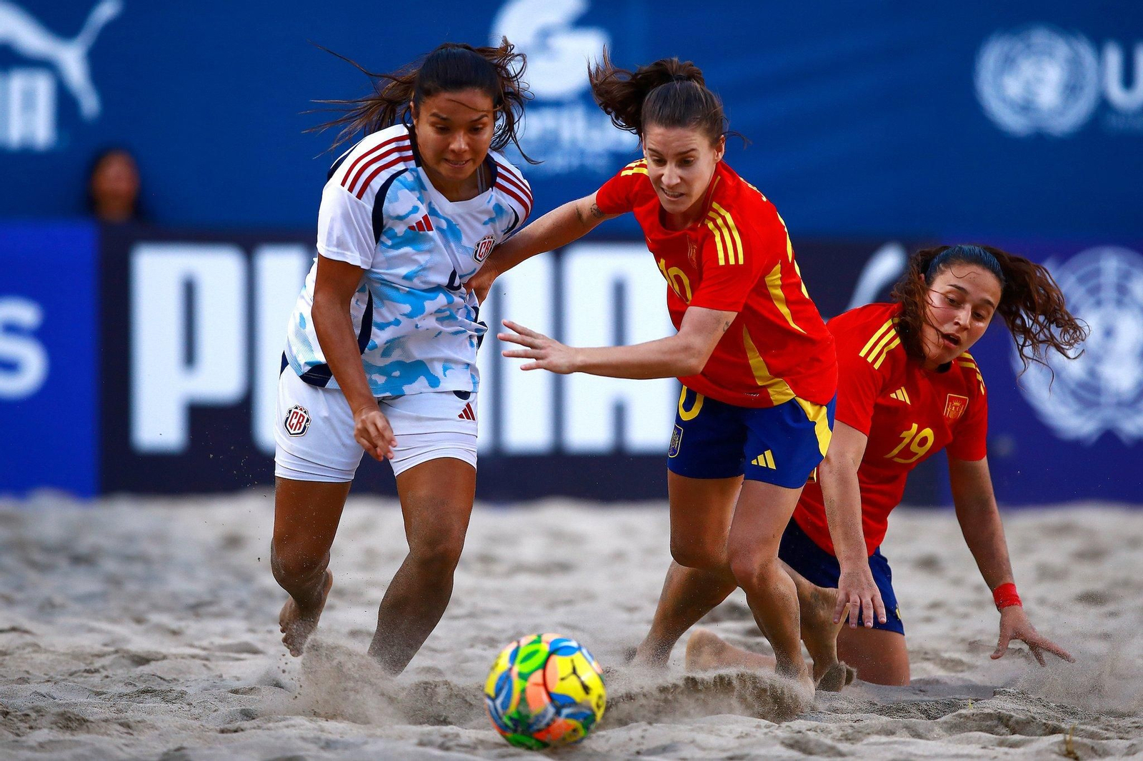 Jessi disputa un balón ante una rival con Paqui de rodillas en la arena en el encuentro frente a Costa Rica.