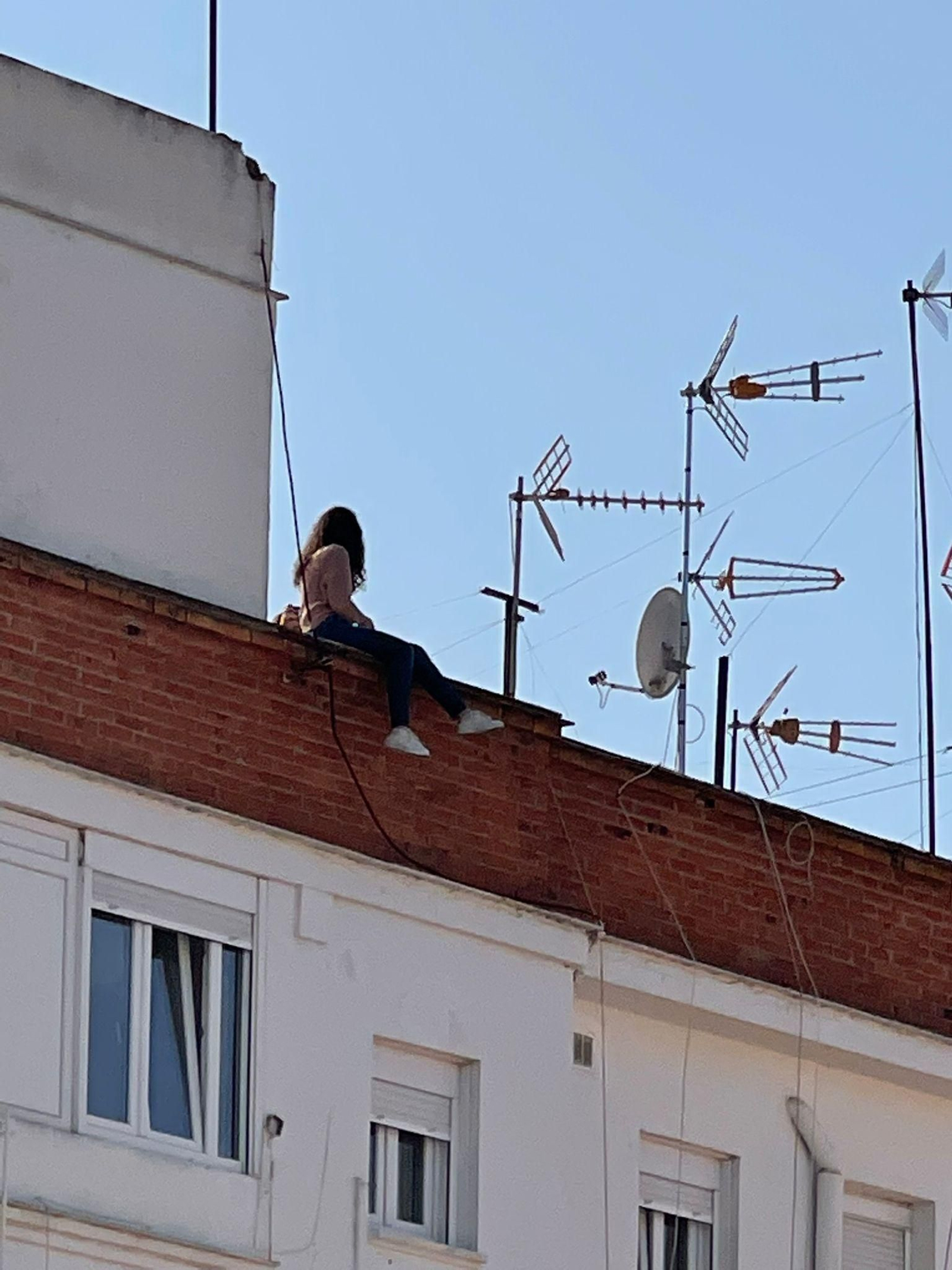 La chica, con los dos pies hacia fuera en la azotea.