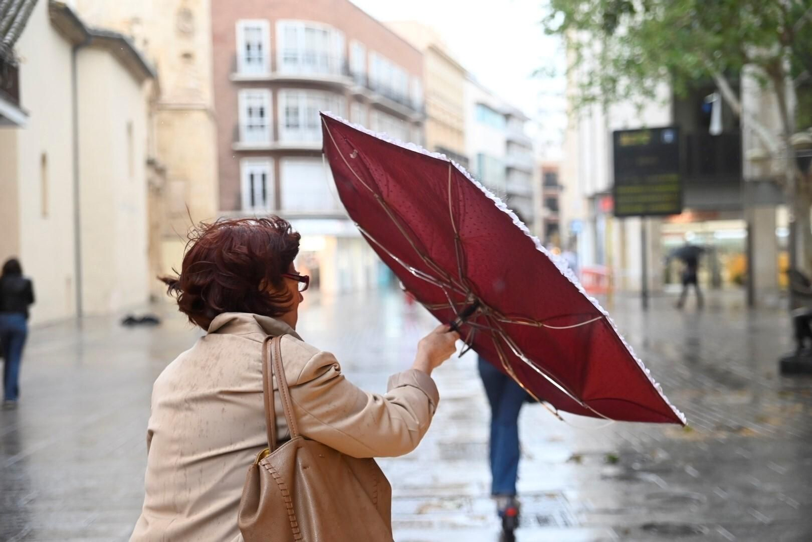 Una mujer sujeta un paraguas volteado por el viento. Una mujer sujeta un paraguas volteado por el viento.