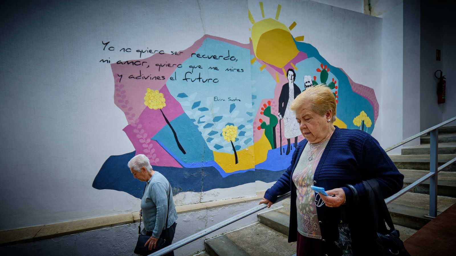 Una señoras se encaminan hacia el Mercado de Abastos mientras pasan por delante de un poético mural.