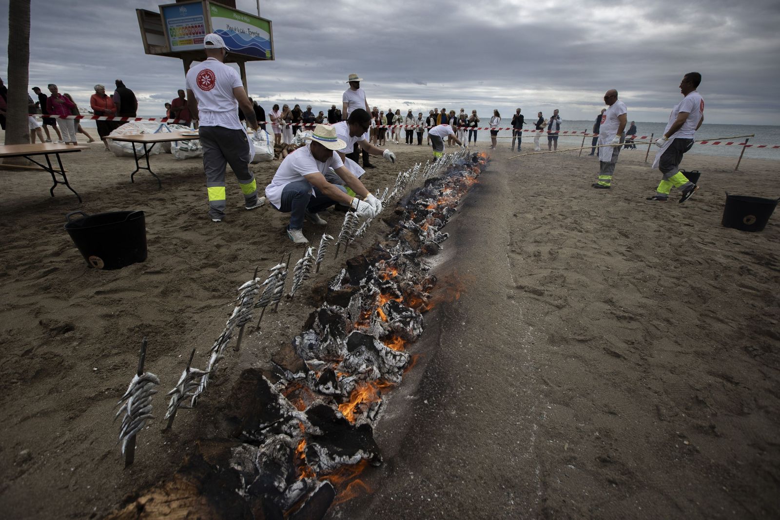 Varios espeteros manipulan las sardinas junto a las brasas