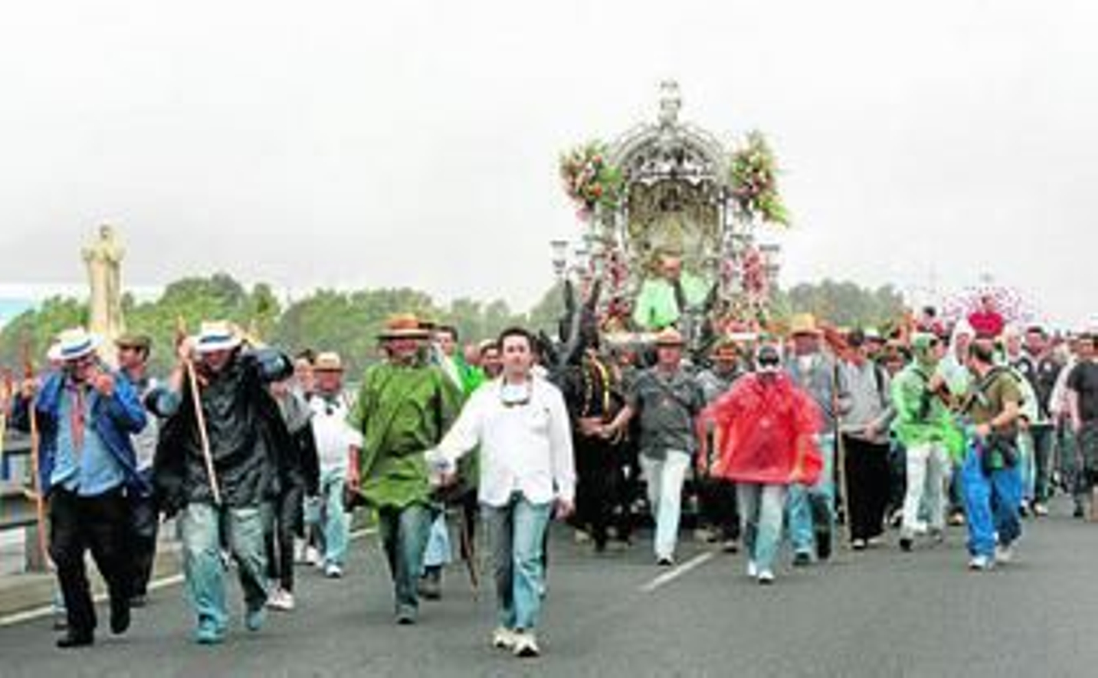 El paso de Emigrantes por el puente de la Punta del Sebo bajo la lluvia y el viento obligó a proteger el Simpecado y a cubrirse los peregrinos que lo acompañaban.