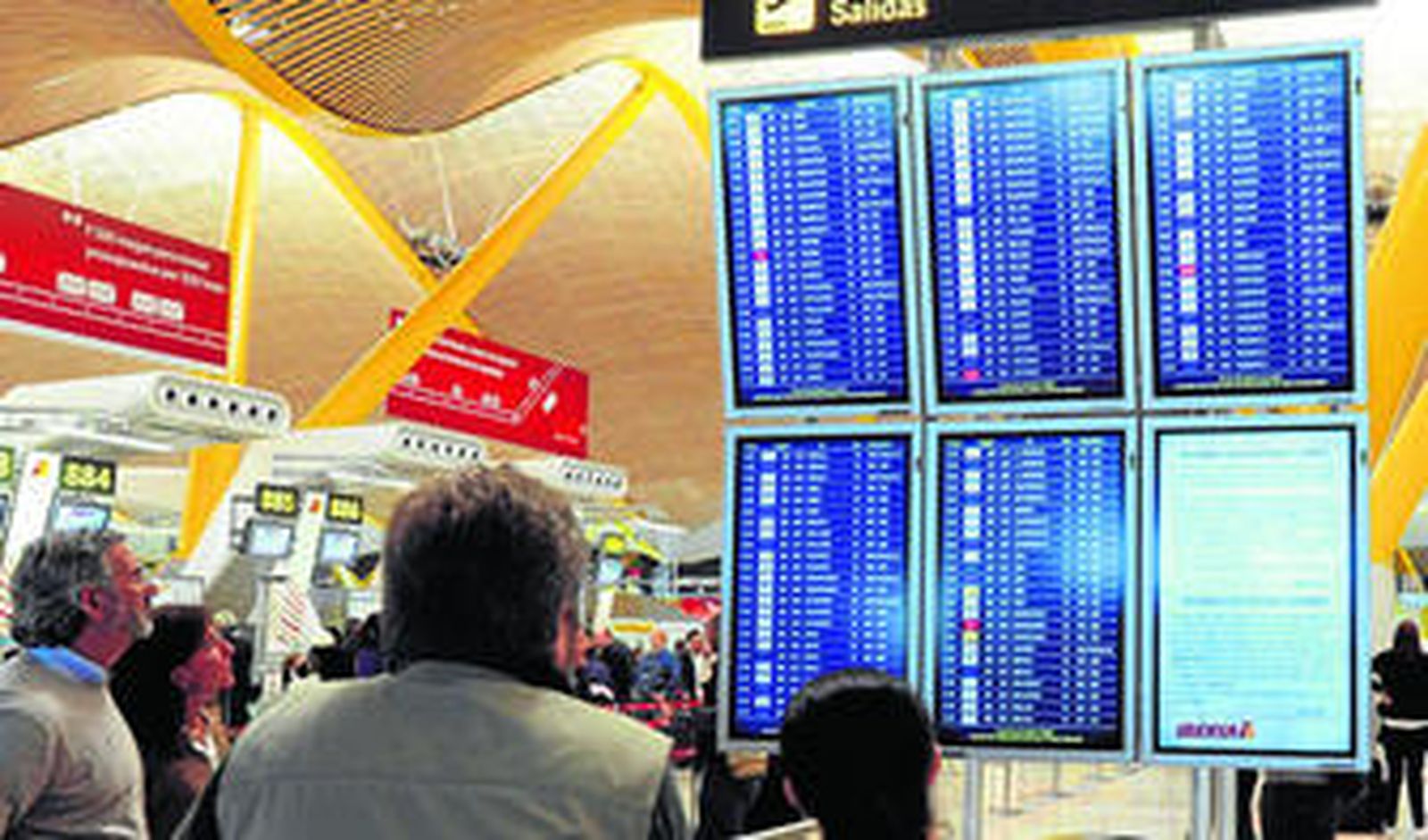 Viajeros atentos a las pantallas de salidas y llegadas de aviones en el aeropuerto de Barajas en Madrid.