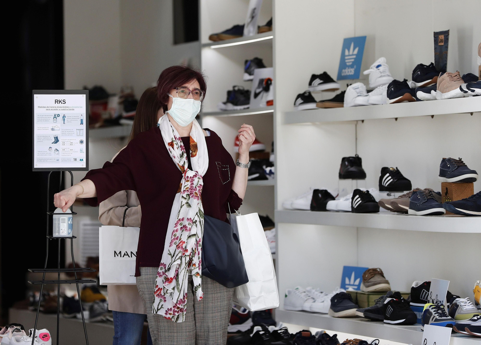 Una mujer sale de una zapatería lavándose las manos con gel