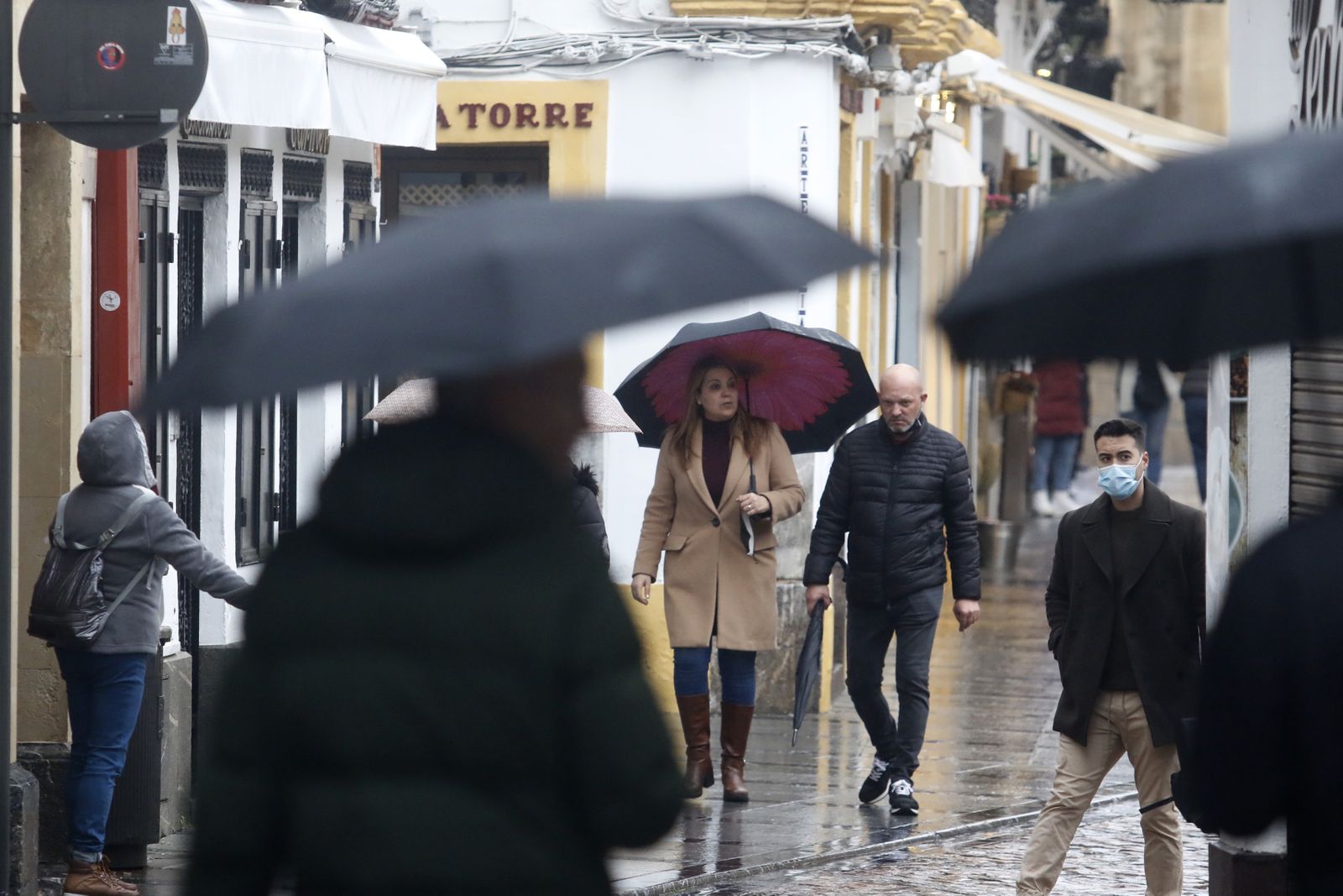 Varias personas caminan por la zona de la Judería bajo la lluvia.