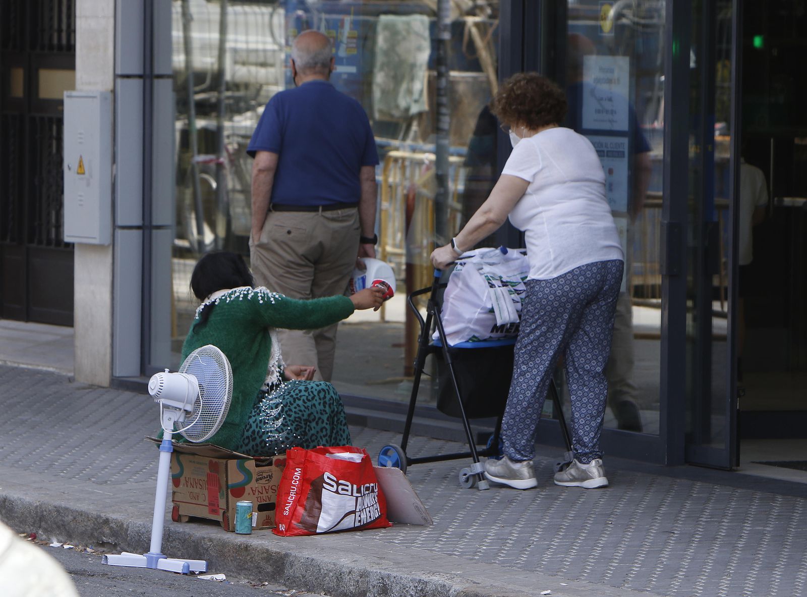 Una persona pide limosna a dos viandantes en una calle de Sevilla.