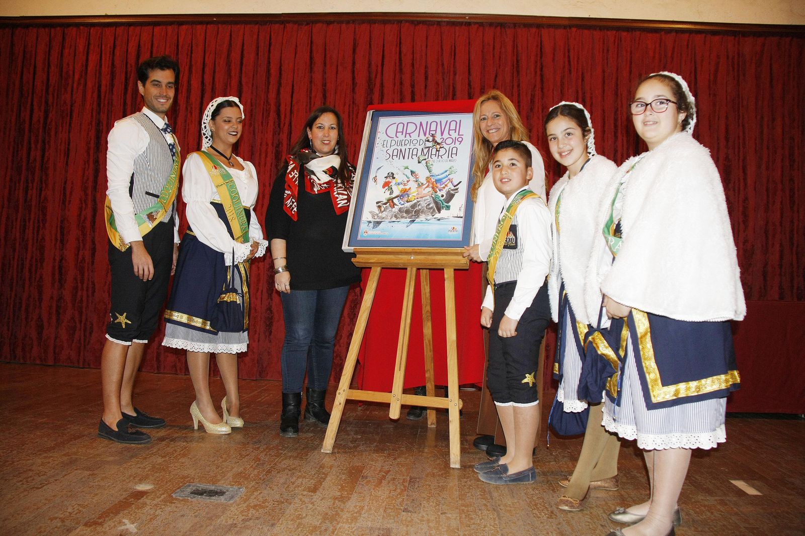 María Eugenia Lara y (izda.) y Ana María Arías (dcha.) junto a los coquineros del año 2018 en el momento de descubrir el cartel anunciador del Carnaval de El Puerto 2019.